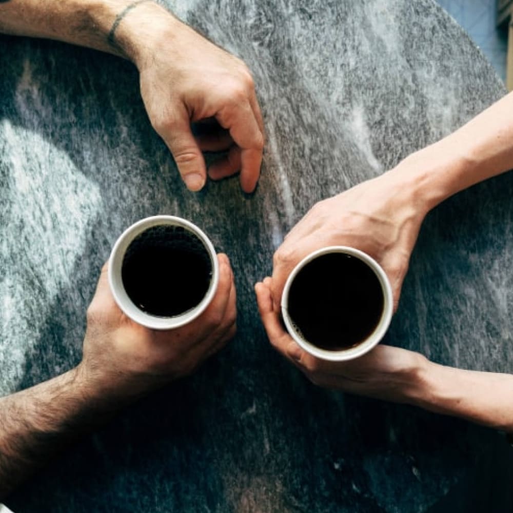 Two sets of hands. Each is holding a white mug full of black coffee.